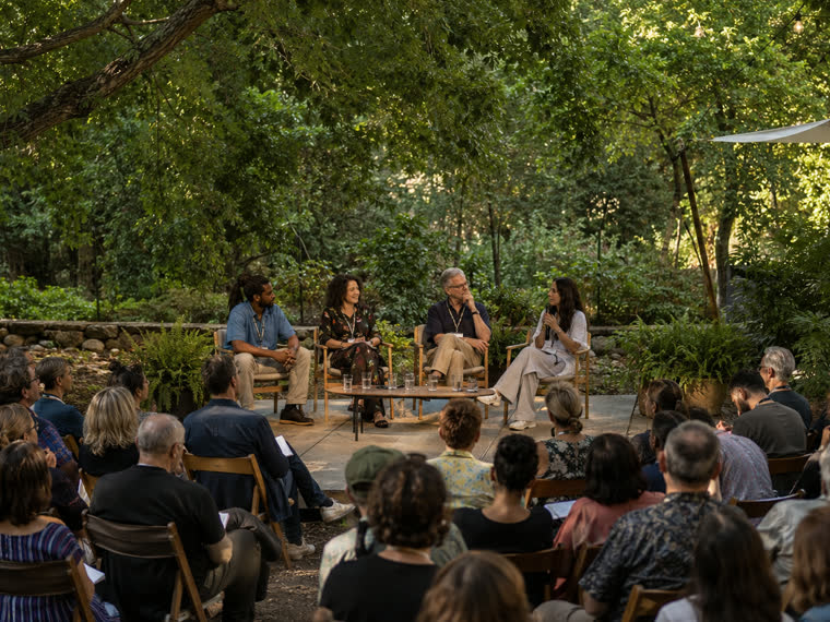 An outdoor panel discussion in front of a seated audience.